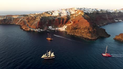 Video-De-Vista-Aérea-De-Drones-De-Hermosos-Veleros-Navegando-En-El-Profundo-Mar-Egeo-Azul-Oscuro-Durante-La-Puesta-De-Sol,-Santorini,-Cícladas,-Grecia