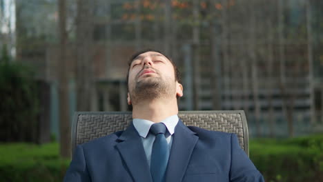 stressed tired businessman leaning back in chair outdoors in a city park - portrait