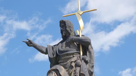 statue of a bearded figure holding a cross against a blue sky
