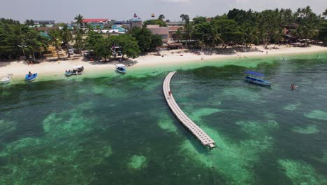 4k drone video of a man running along a long plastic jetty from alone beach in bohol, philippines