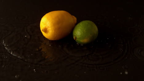 limón y lima cayendo sobre una superficie negra húmeda
