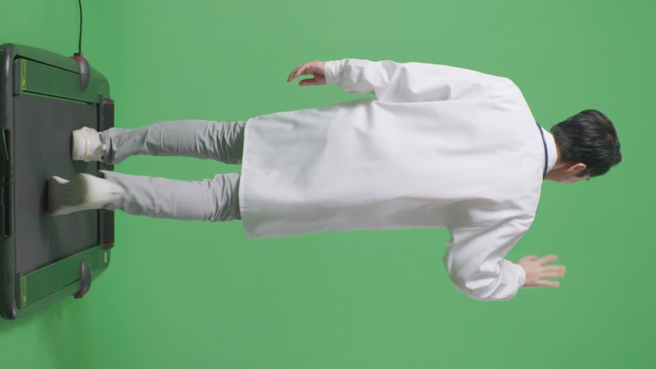 스테토스코프를 들고 있는 아시아 남성 의사가 병원에서 녹색 스크린 배경에서 는 동안 손을 흔들고 미소 짓고 있다.