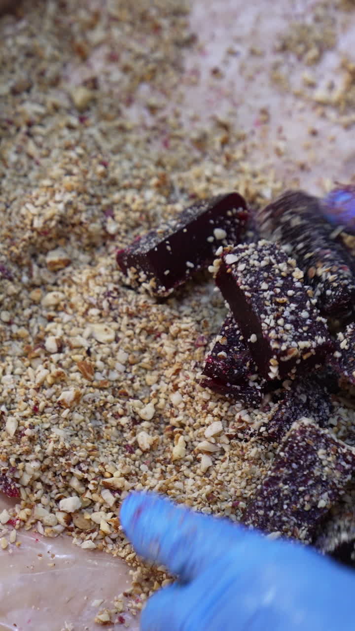 Marmalade bars being covered with mashed nuts. Worker's hands in gloves mix pieces of jelly candies with hazelnuts. Vertical video