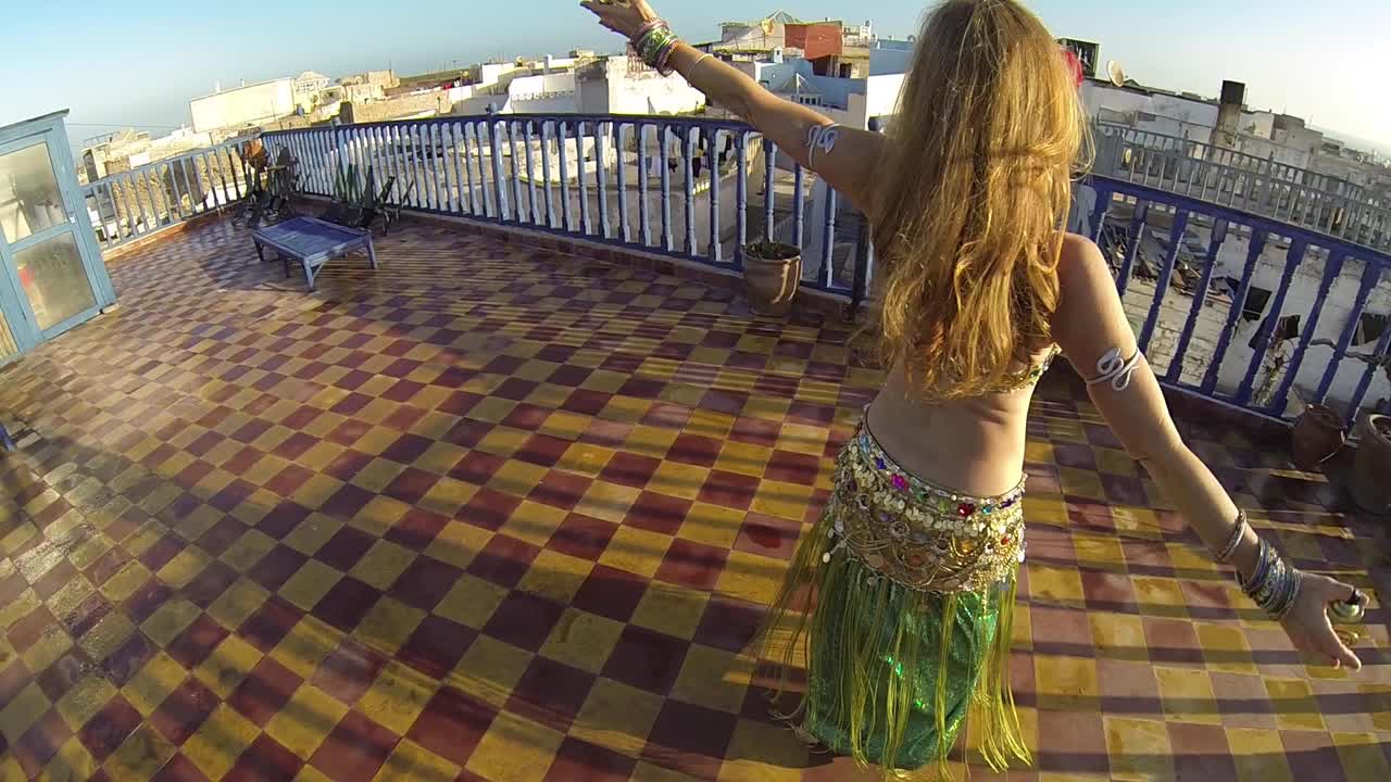 High angle looking down on belly dancer as she spins on the roof of a building in Morocco at sunset