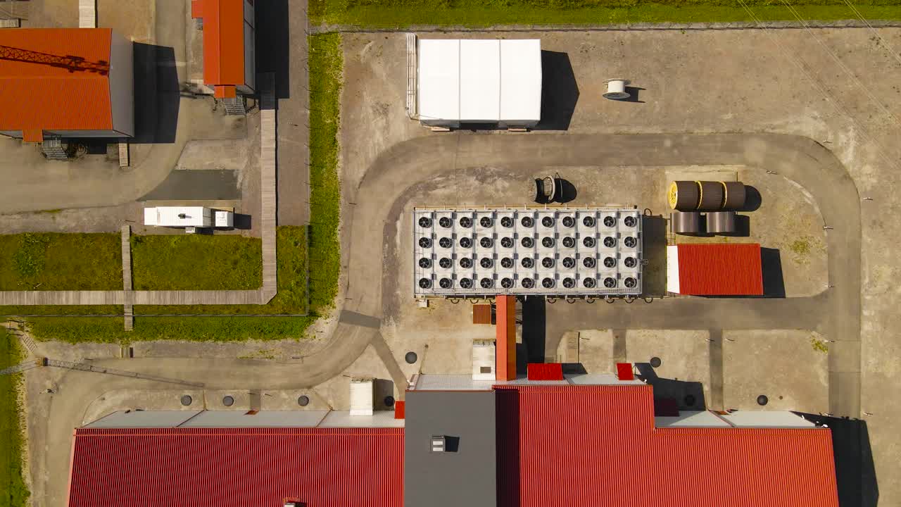Aerial drone footage flying lower and descending upon a modern electrical sub station that has massive cooling system fans spinning next to it at sunny day. Cooling and powering data center and server
