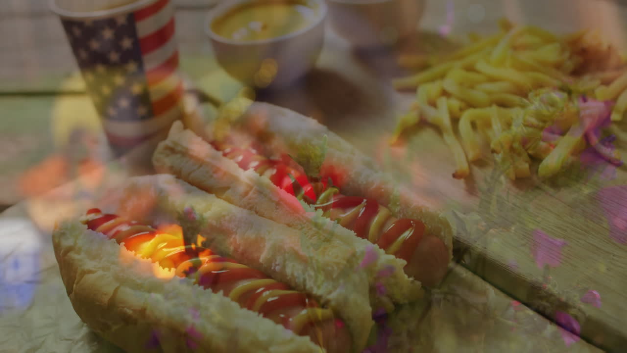 On table, hot dogs with ketchup and mustard, fries, American flag cup