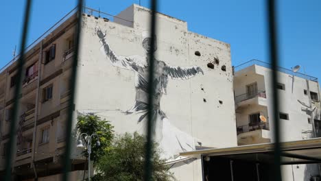 pov seeing large wall painting on side of building seen through railings