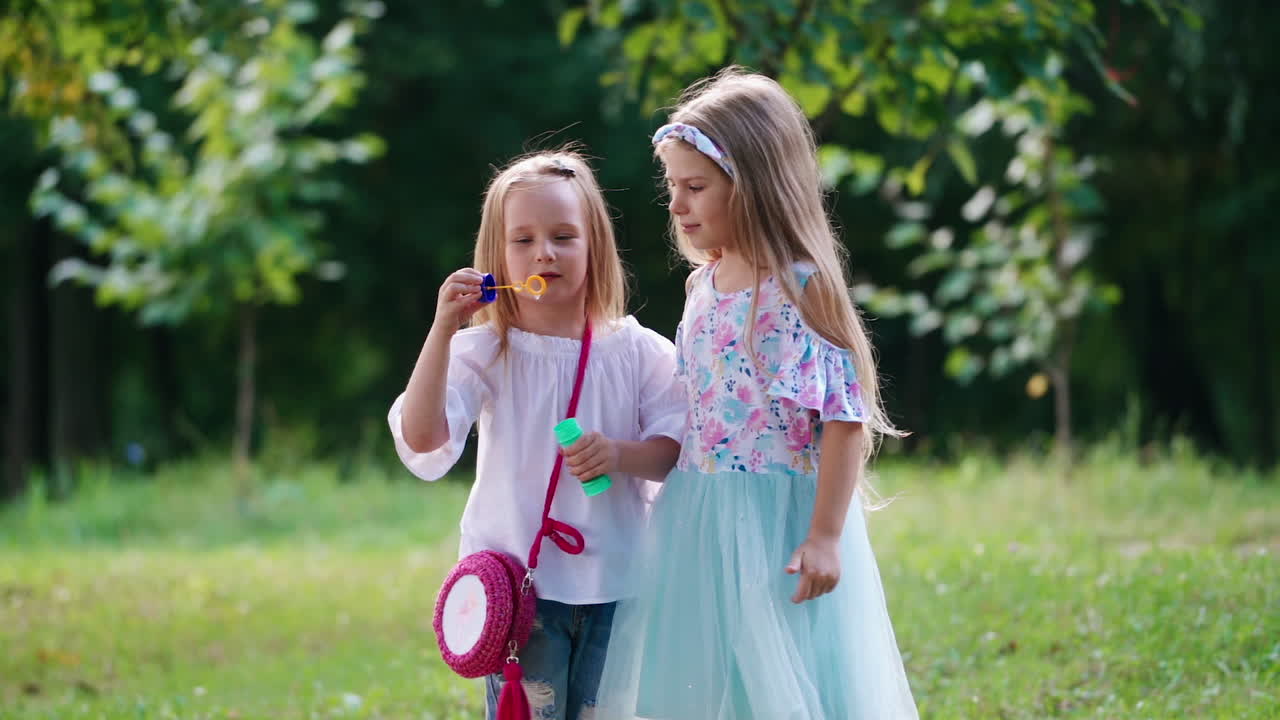 Little girls with bubble blower outside. Two lovely girls playing together with soapy bubbles in the park in summer.