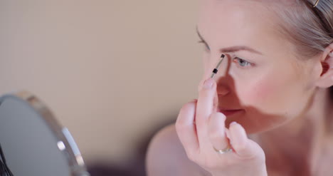 mujer haciendo maquillaje pintando pestañas con rímel