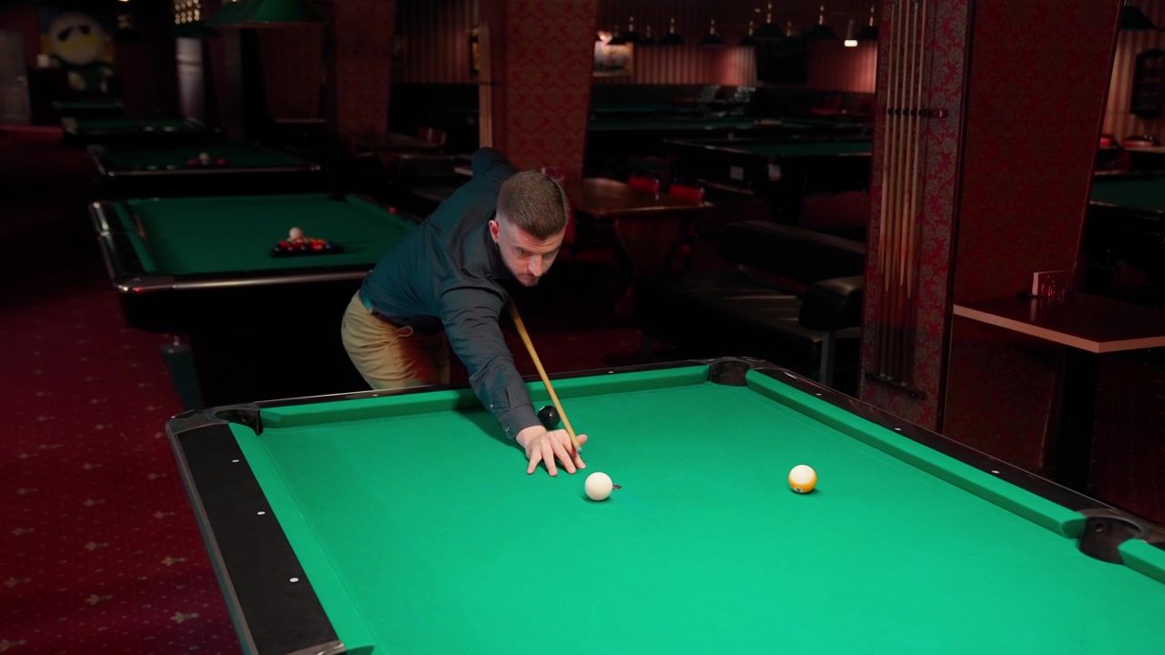 Jonge man die biljart speelt en de speelbal stoot in een donkere poolzaal