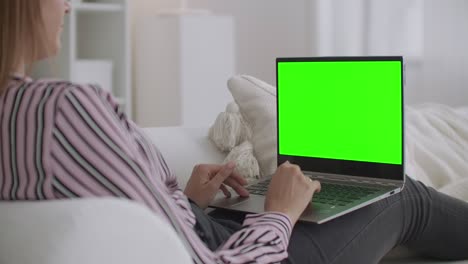 mujer estudiante está chateando en línea por computadora portátil con pantalla verde para la tecnología de clave de croma, descansando en casa los fines de semana