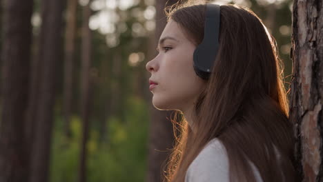 lady with headphones rests by tree at sunset. desperate woman copes with depression walking in dense forest in evening. finding emotional release