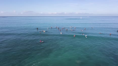 crowd of surfers at waikiki beach honolulu hawaii with a pan reveal of mountains and honolulu city, aerial trucking pan