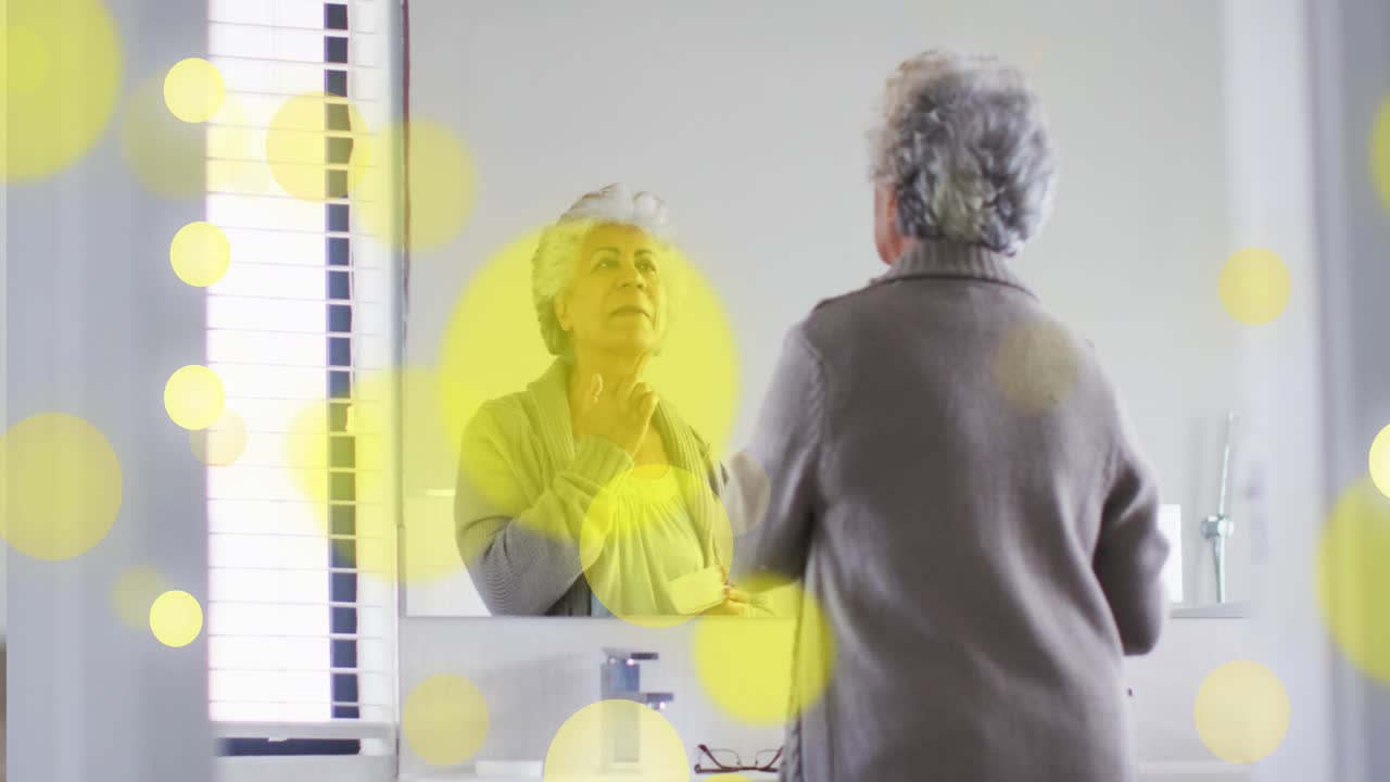 Mother and daughter doing skincare at vanity picking jar applying cream, yellow bokeh hiding faces