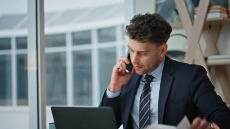 Company worker complaining smartphone call sitting laptop work desk closeup