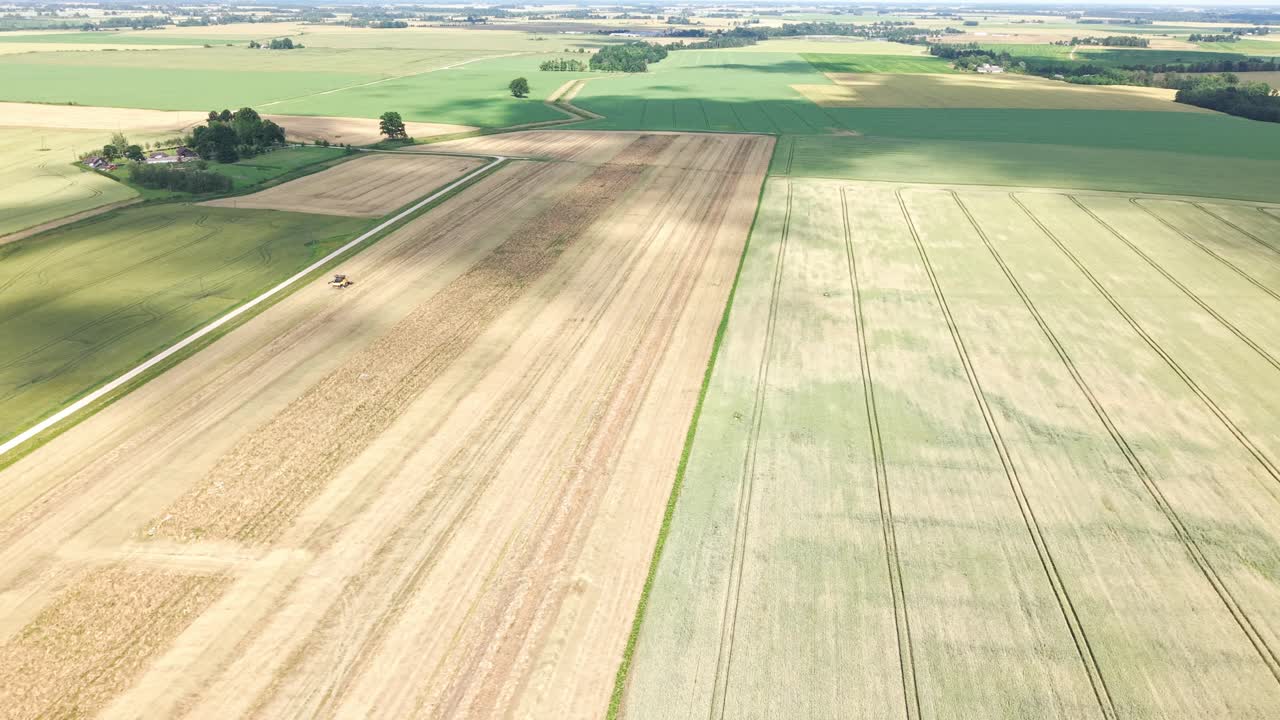 Aerial pan of green and golden crop fields with visible tractor path lines and machinery