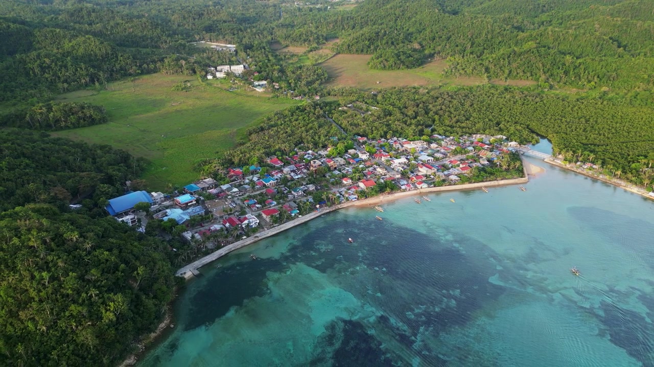 Ripresa aerea in allontanamento su un villaggio costiero rurale, barriere coralline poco profonde, colline lussureggianti e acque limpide - Magnesia Del Norte, Catanduanes, Filippine.