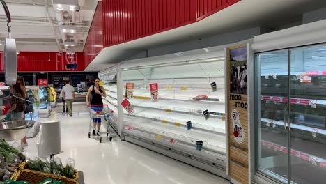 a shopper in australia passes empty supermarket shelves during coronavirus (covid-19) panic buying.