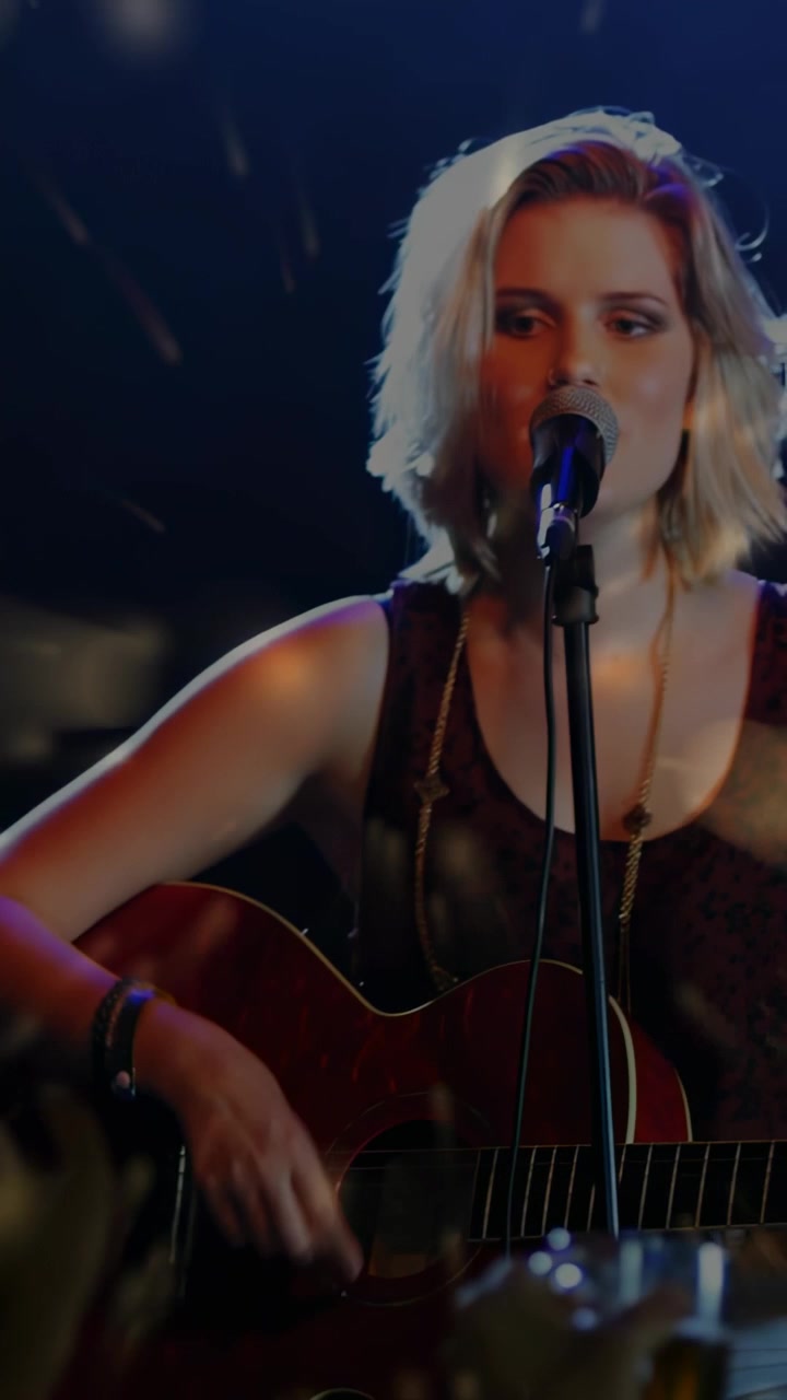 Camera focusing, female singer in sleeveless top strumming acoustic guitar, singing for club, glass