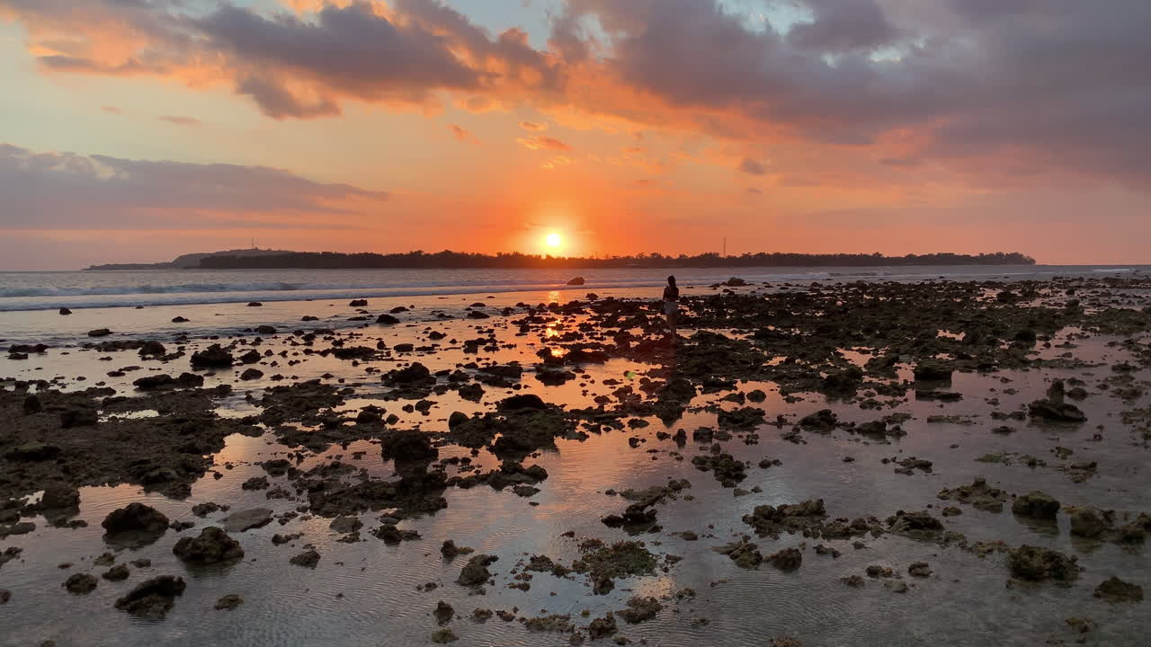 puesta de sol naranja dorada desde gili air de gili meno con silueta de mujer viajando caminando a través de rocas de marea baja