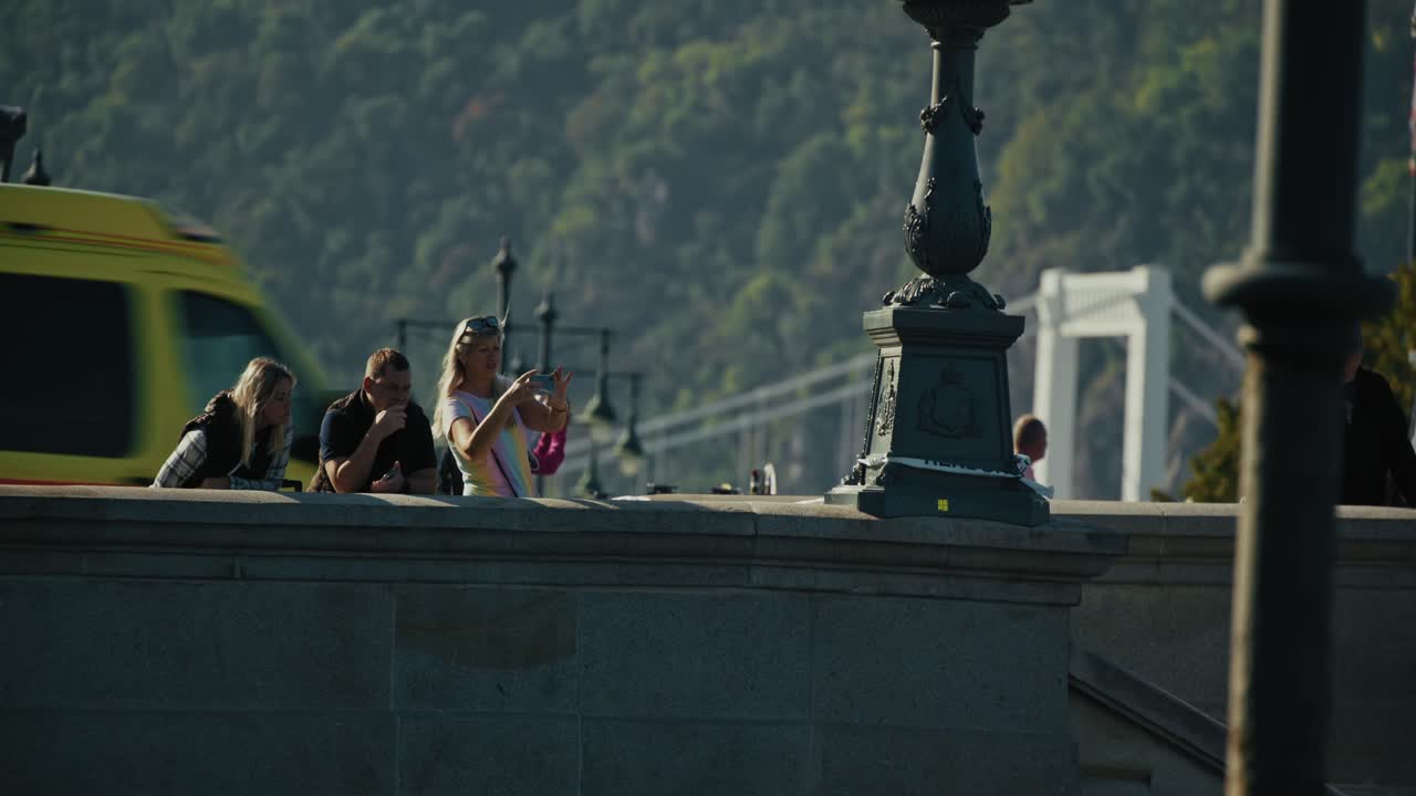 Group of people relax on a bridge overlooking a scenic view on a sunny day, Budapest Hungary