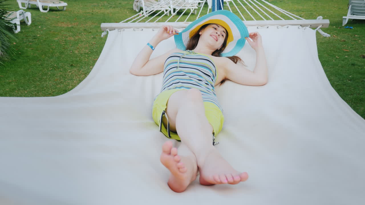 una joven con un sombrero fresco y brillante está disfrutando del descanso en una hamaca blanca en un balneario