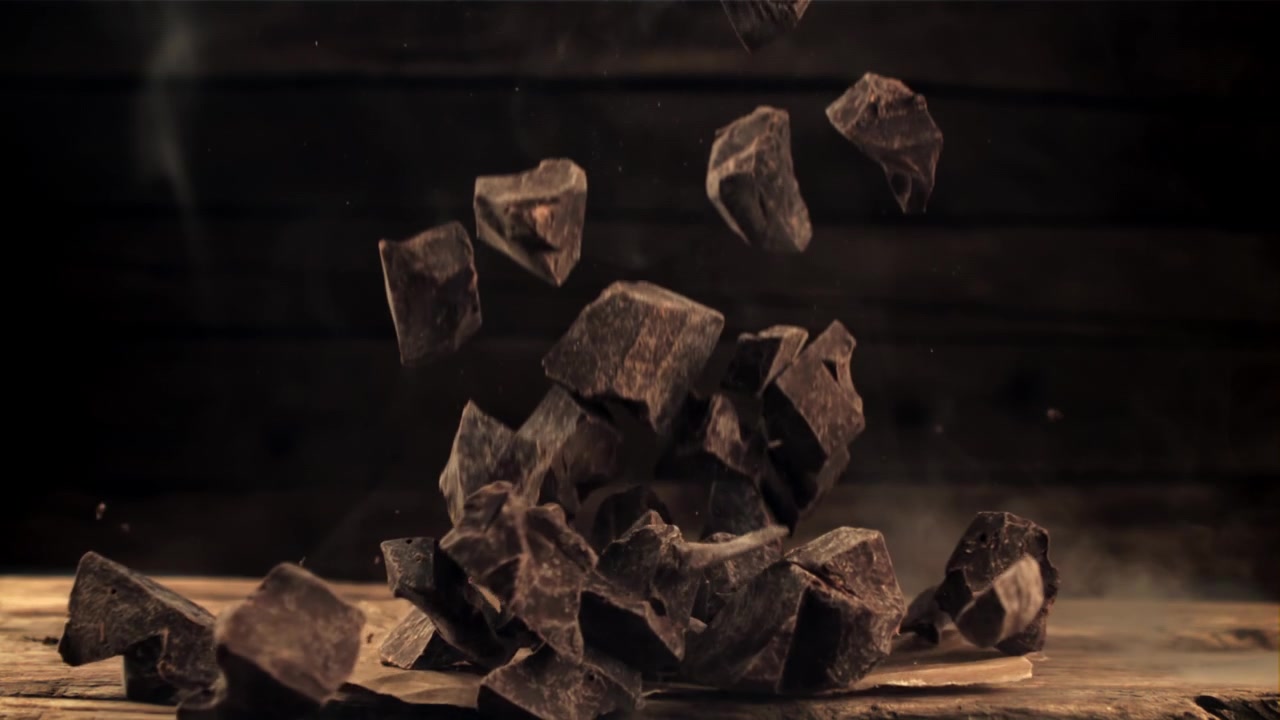 Deliciosos trozos de chocolate negro cayendo sobre una mesa de madera rústica