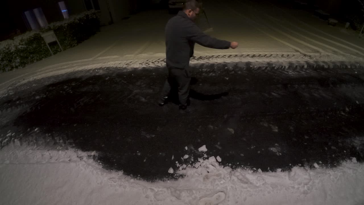Un uomo sparge sale su una superficie ghiacciata di notte per evitare di scivolare. Concetto di sicurezza invernale, controllo del ghiaccio, prevenzione degli incidenti e manutenzione responsabile in condizioni di freddo