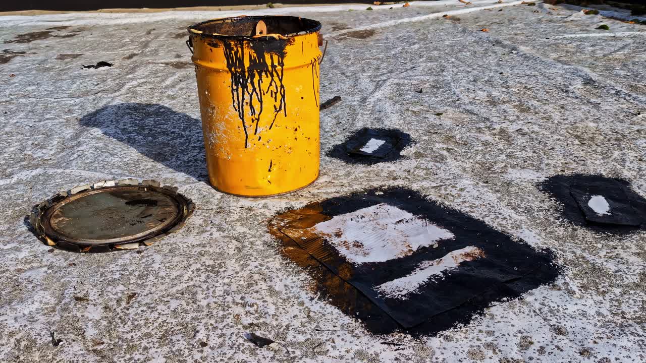 Secchio giallo sporco e chiazze di catrame su un tetto piano bianco durante i lavori di impermeabilizzazione