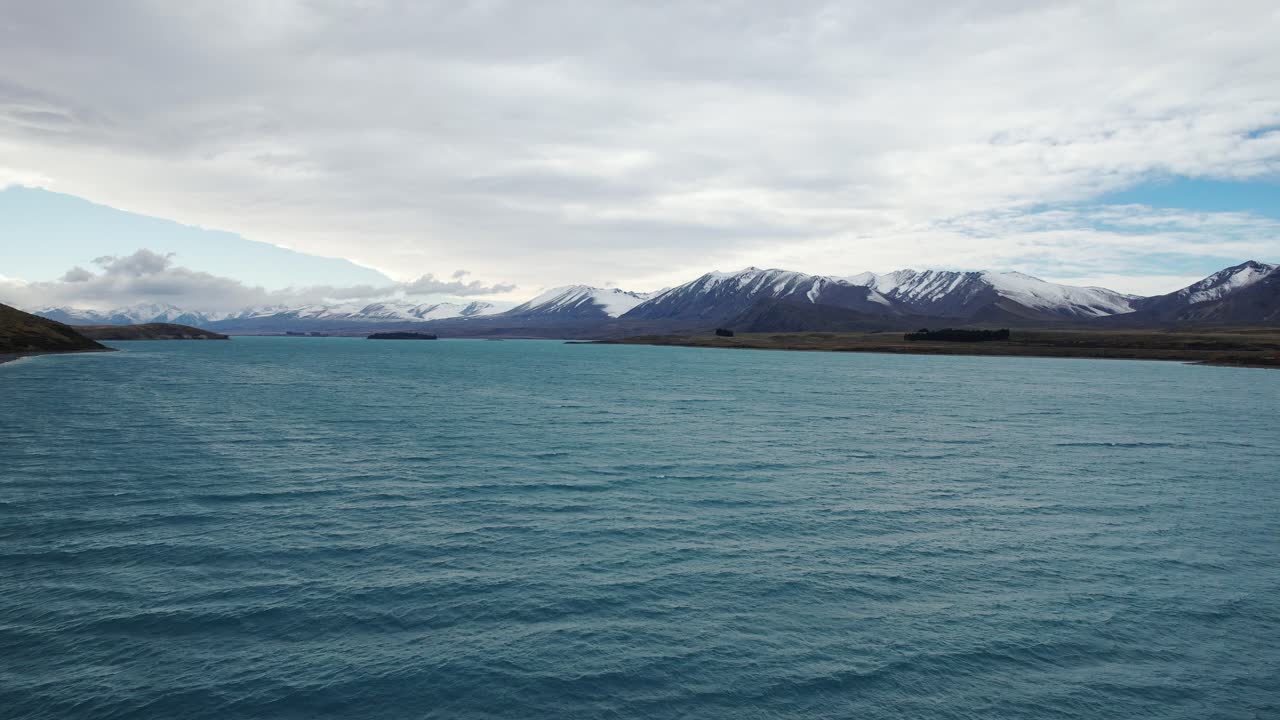 Flying Over The Lake Tekapo With Snowy Mountains In The Distance In South Island, New Zealand. - aerial shot