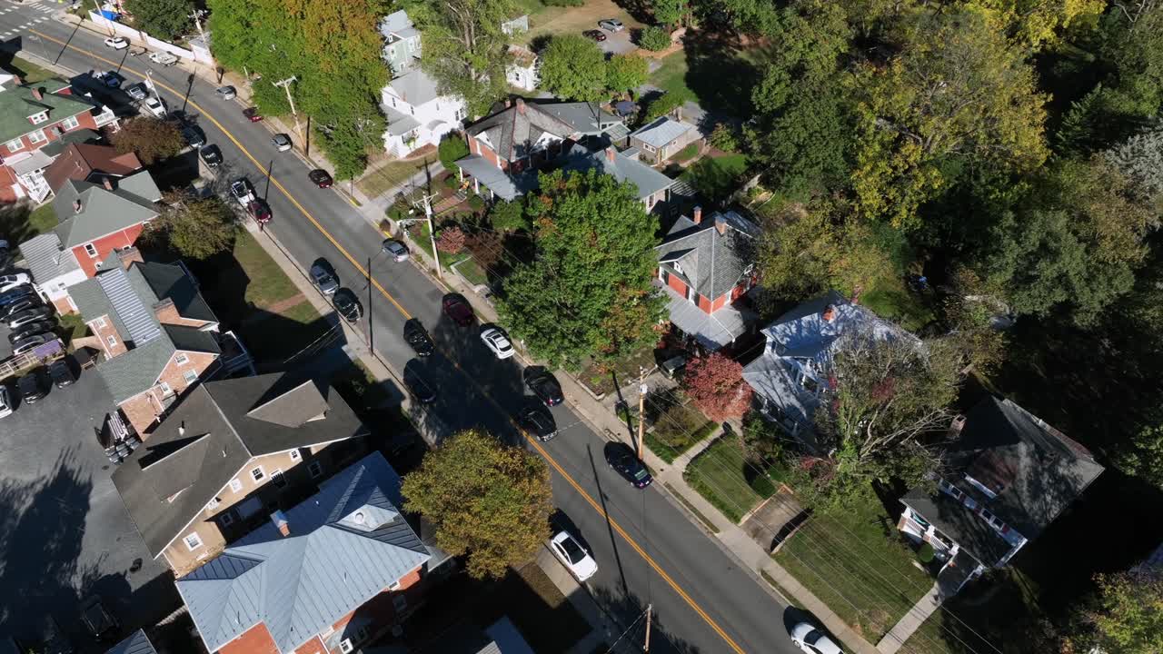 Driving cars on street of suburb neighborhood with colonial and victorian houses in USA. Sunny day in fall season. Peaceful and quiet scene in suburbia, Virginia. Drone top down shot
