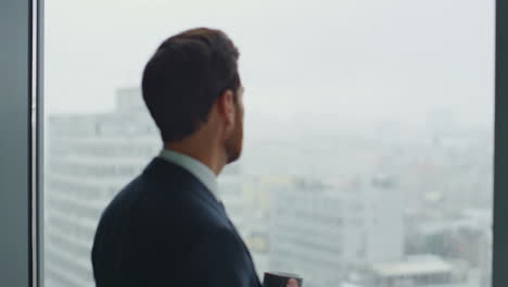 serious director drinking coffee looking on office window cityscape close up.