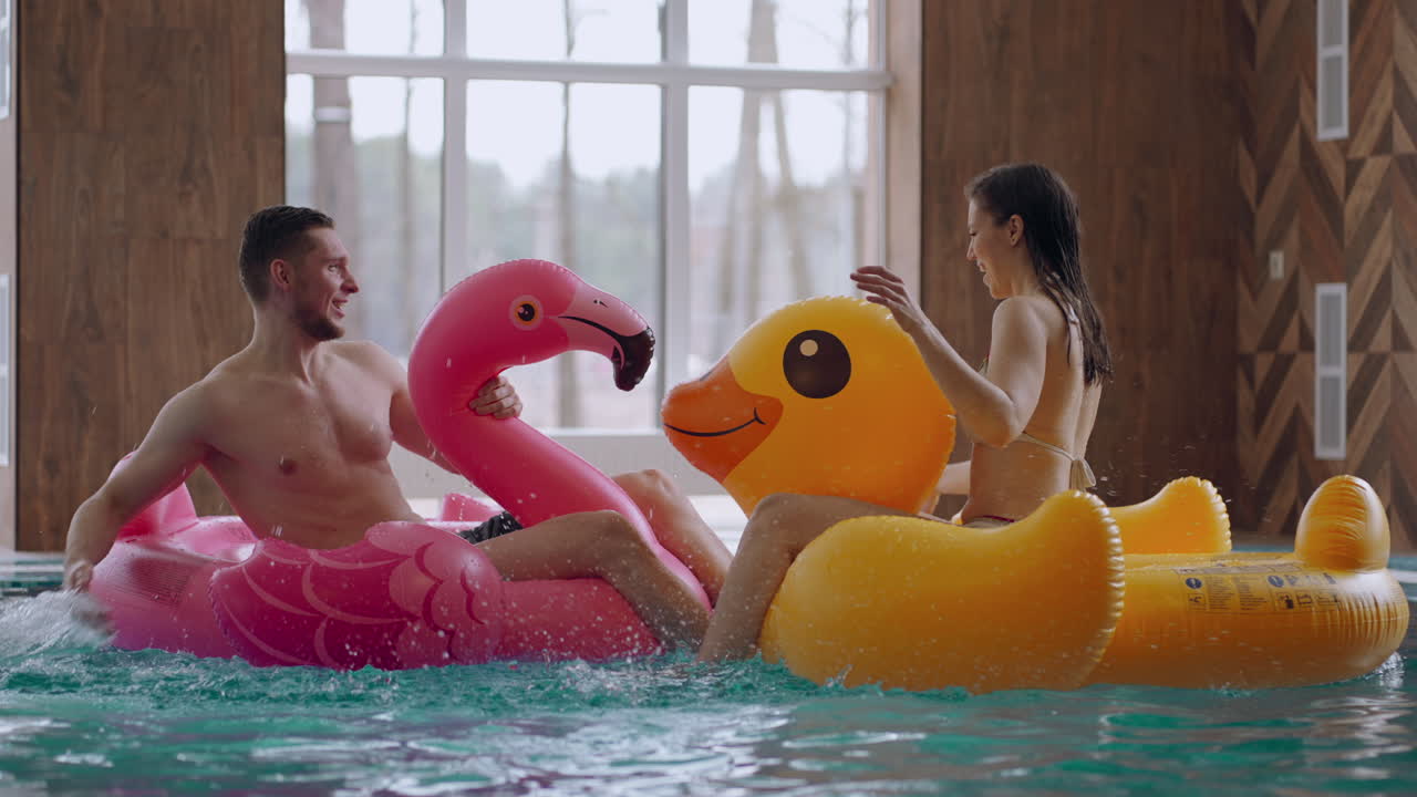 esposa y marido se están divirtiendo en un parque acuático o piscina pública sentados en divertidos círculos inflables y salpicando agua