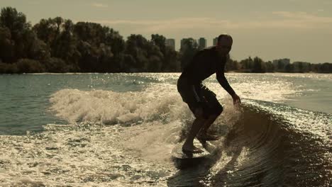deportista montando en wake surf al atardecer. hombre deportivo entrenando en tabla de surf