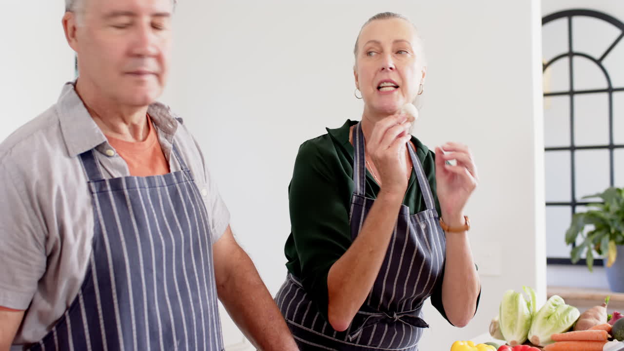 Senior friends in kitchen, woman explaining cooking technique to man