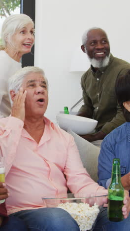 happy senior diverse people watching tv with beer at retirement home