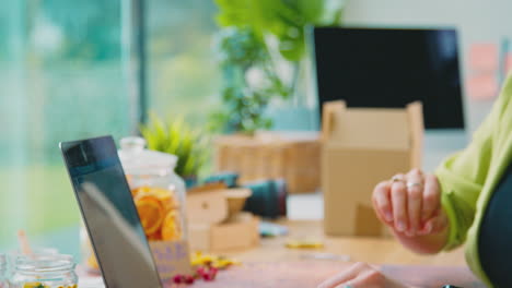 woman with laptop running online business making candles at home