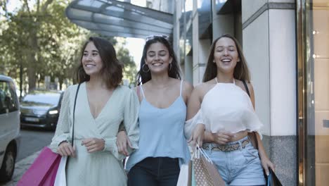 Three-happy-women-walking-together-and-laughing-with-shopping-bags