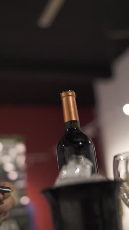 man opens bottle of wine with corkscrew at elegant party reception, on table next to bowl of ice