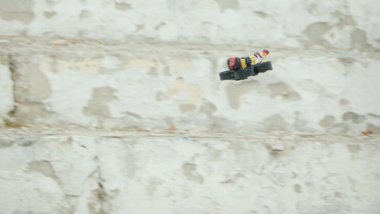 Un drone sportivo con telecamera vola velocemente contro una parete bianca: ripresa in movimento