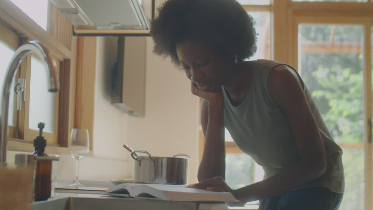 African American Woman Reading Book while Cooking Food