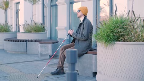 visually impaired man sitting on the bench in the city.