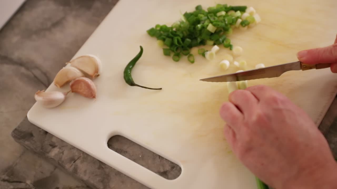 Top-Down View Of Woman Cutting Green Onions Next To Garlic And Chili Pepper In Slow Motion