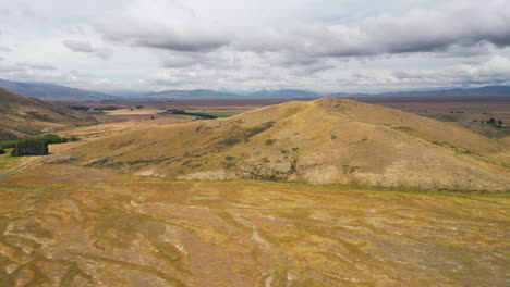 Aerial-drone-forward-moving-shot-over-countryside-highway-leading-through-golden-meadows-in-Central-Otago,-New-Zealand's-southern-Alps