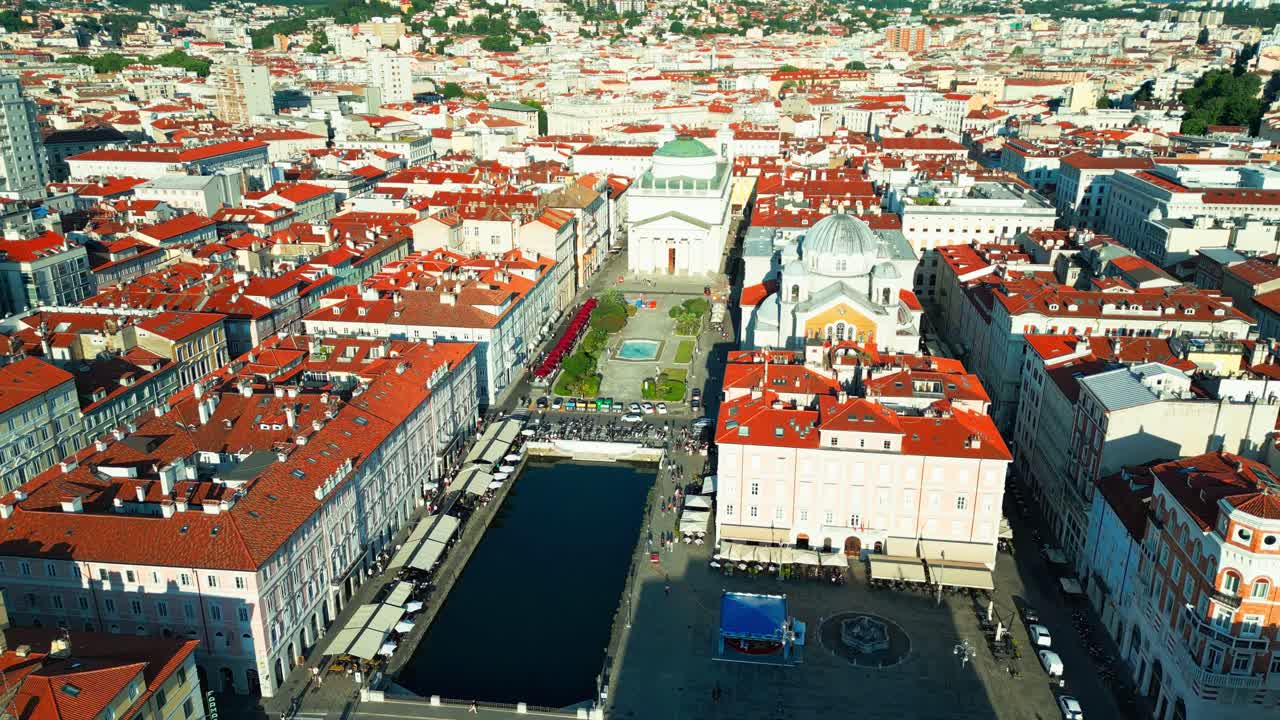 Aerial drone shot of Canal Grande and Piazza Sant’Antonio in Trieste, featuring the iconic Sant’Antonio Taumaturgo Church and vibrant red-roofed architecture.
