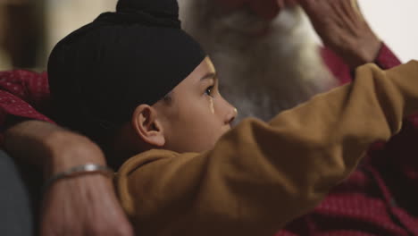 Smiling-Sikh-Grandfather-And-Grandson-Wearing-Turbans-Sitting-On-Sofa-At-Home-Talking-Together-Shot-In-Real-Time