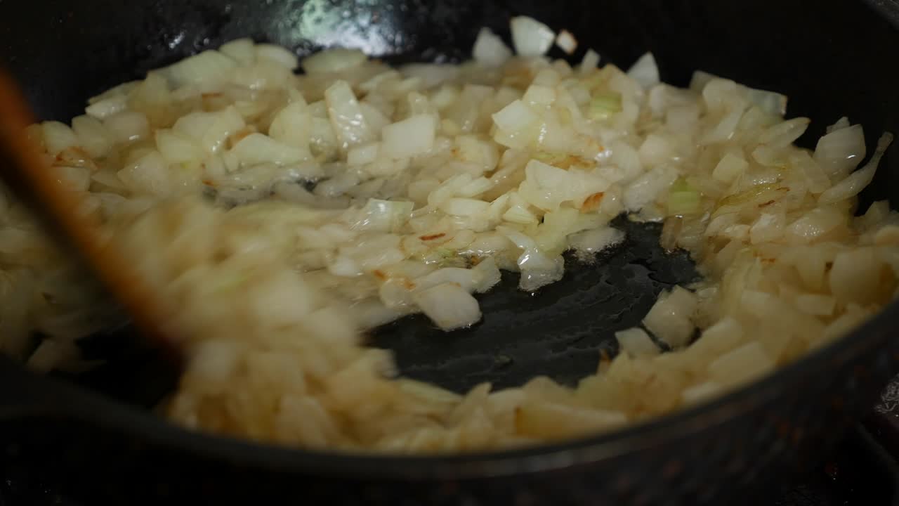 Frying onions in a pan with oil. Stir onion in skillet with wooden spatula