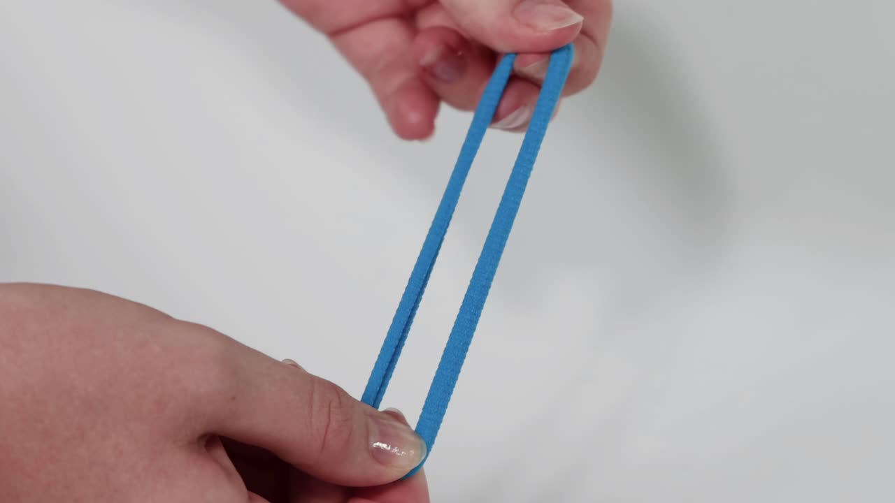 Close-up of hands stretching and manipulating a blue elastic band against a white background.