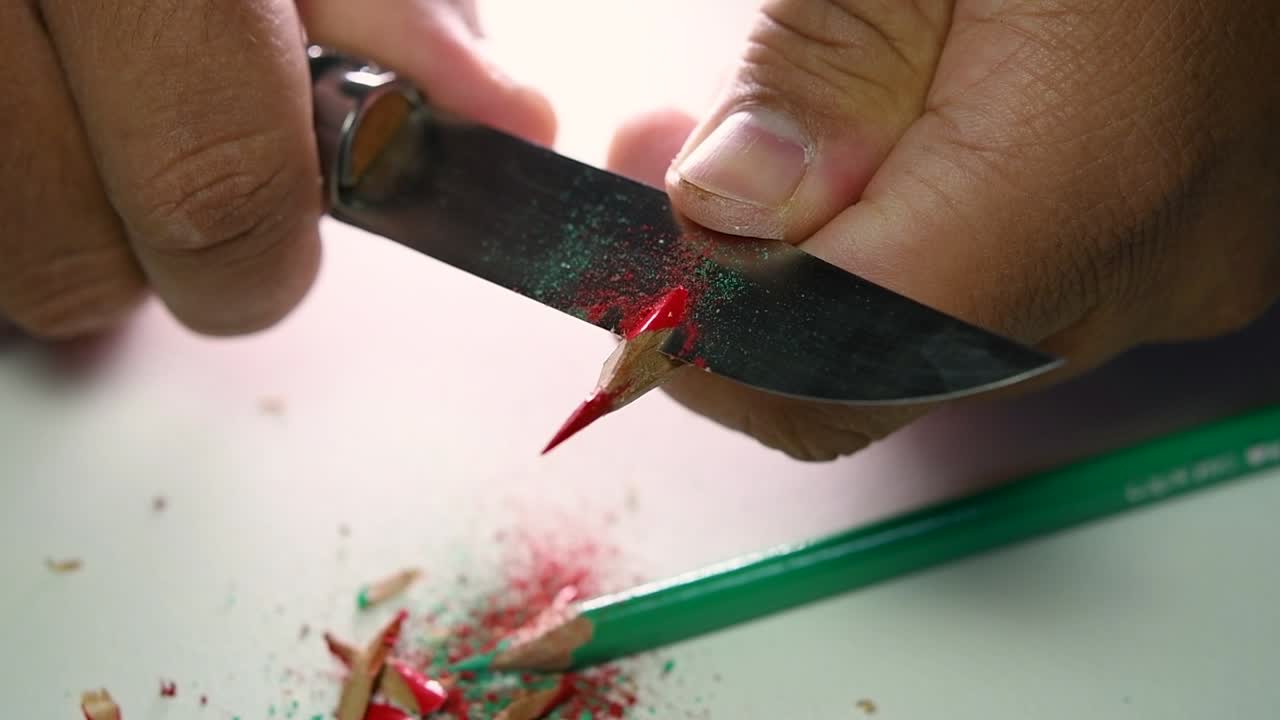Opptak av hender som sakte spisser en blyant og noen fargeblyanter med en skarp kniv
