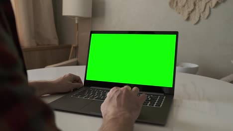 hombre trabajando en una computadora portátil con pantalla verde. quédate en casa. vista sobre el hombro.